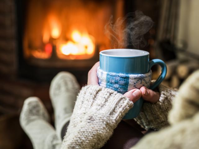 person holding steaming mug in front of a fire place